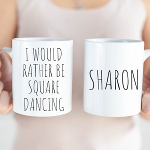 May include: Two white ceramic mugs with black text. One mug says "I would rather be square dancing" and the other mug says "SHARON".