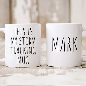 May include: Two white ceramic mugs. One mug says "This is my storm tracking mug". The other mug says "Mark".