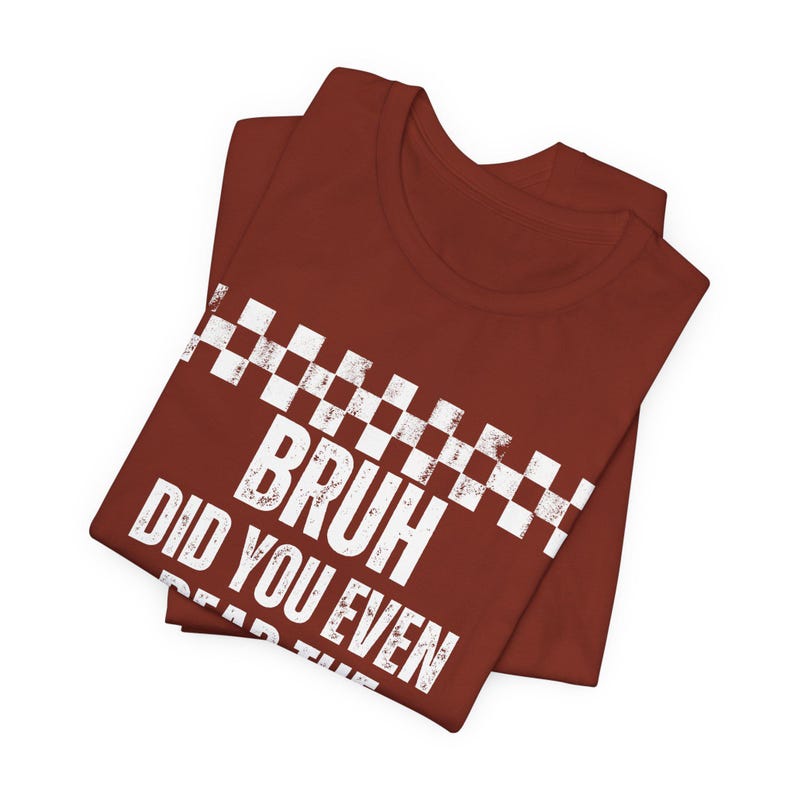 May include: A maroon t-shirt featuring the white text "BRUH DID YOU EVEN READ THE" and a white and black checkered design. The shirt is folded, suggesting it's new and made of a soft fabric.