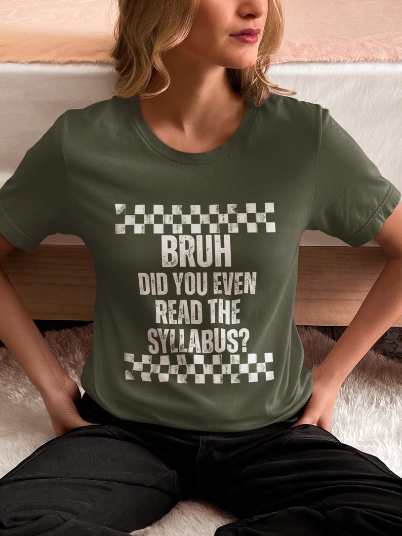 May include: An olive green t-shirt featuring the white text "BRUH DID YOU EVEN READ THE SYLLABUS?" with a checkered design above and below. The shirt has short sleeves.