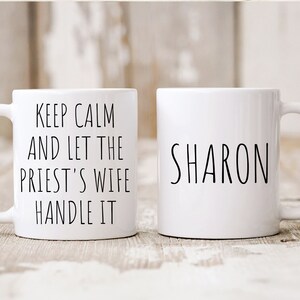 Peut inclure: Deux tasses en c&eacute;ramique blanche. Une tasse porte le texte "Keep Calm and Let the Priest's Wife Handle It" et l'autre tasse porte le nom "SHARON" imprim&eacute; dessus.