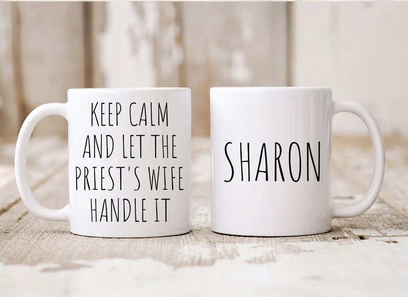 Peut inclure: Deux tasses en c&eacute;ramique blanche. Une tasse porte le texte "Keep Calm and Let the Priest's Wife Handle It" et l'autre tasse porte le nom "SHARON" imprim&eacute; dessus.