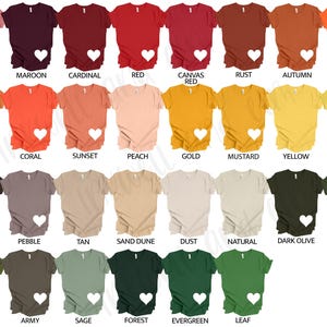 May include: A selection of V-neck t-shirts in a variety of colours, such as mauve, maroon, and red. Each shirt features a white heart design. The colour palette includes warm tones like orange and gold, alongside cooler shades like green and olive.