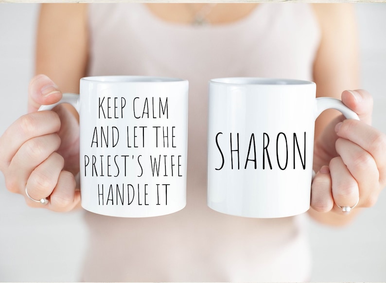 Peut inclure: Deux tasses en c&eacute;ramique blanche. Une tasse dit "Keep Calm and Let the Priest's Wife Handle It". L'autre tasse dit "Sharon".