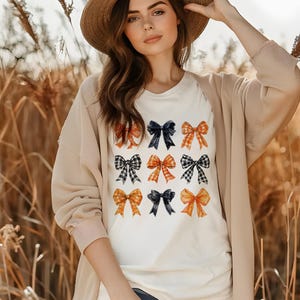 May include: A white t-shirt with a pattern of nine orange, black, and white plaid bows. The bows are arranged in a 3x3 grid.