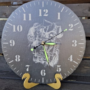 Könnte beinhalten: Eine graue Schieferuhr mit einem Schwarzweißbild eines Piraten-Schädels und Knochen. Die Uhr hat schwarze Zeiger und einen goldenen Ständer.