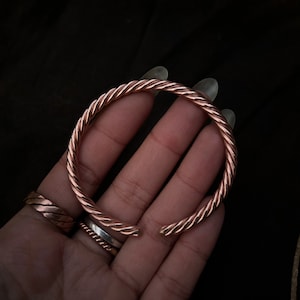 May include: A copper bracelet with a twisted design. The bracelet is open and has a smooth, polished finish.