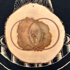 Puede incluir: Dos aros de alambre de cobre, retorcidos y superpuestos, sobre una superficie de madera.