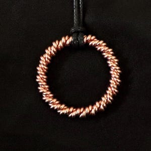 May include: A copper necklace with a coiled circle pendant. The pendant is a simple, continuous circle of copper wire.