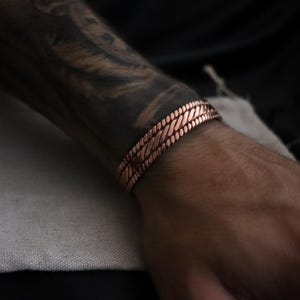 May include: A copper bracelet with a braided design. The bracelet is worn on a person's wrist.