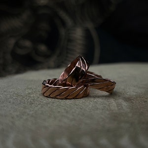 May include: Three copper rings with a braided design. The rings are stacked on top of each other.