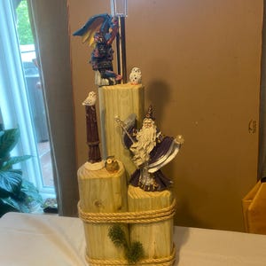 以下が含まれることがあります： 木製の柱の上に魔法使い、ドラゴン、フクロウが乗った、気まぐれなソーラーガーデンライト。ライトは透明なチューブと黒い上部を備えています。木製の柱はロープで結ばれ、緑で飾られています。高さ約30cm。