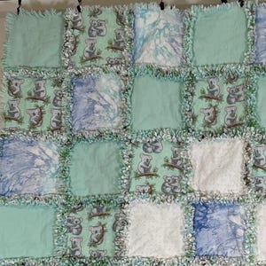 May include: A handmade patchwork quilt with a koala bear pattern. The quilt features squares of light blue, white, and patterned fabric. The quilt is approximately 50 inches by 50 inches.