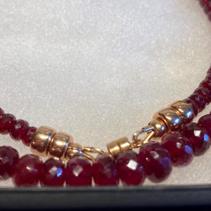 以下が含まれることがあります： 赤い宝石のビーズと金の留め具でできた、2連のネックレスのクローズアップです。