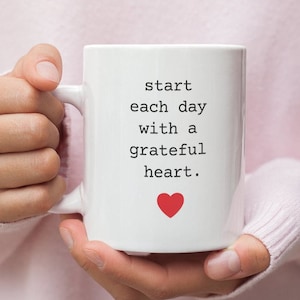 May include: White ceramic mug with a black text that reads "start each day with a grateful heart." A red heart is below the text.