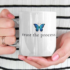May include: White ceramic mug with a blue butterfly graphic and the text "trust the process" printed in black.