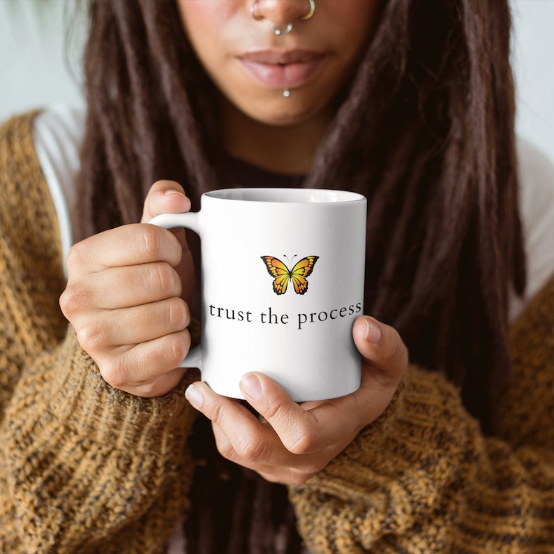 May include: White ceramic mug with a yellow and orange butterfly graphic and the text "trust the process".