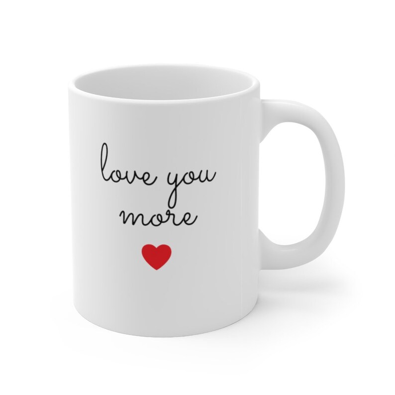 Puede incluir: Taza de caf&eacute; de cer&aacute;mica blanca con texto negro que dice "love you more" y un peque&ntilde;o coraz&oacute;n rojo.