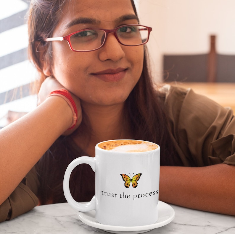 May include: White ceramic coffee mug with a yellow and orange butterfly graphic and the text "trust the process".