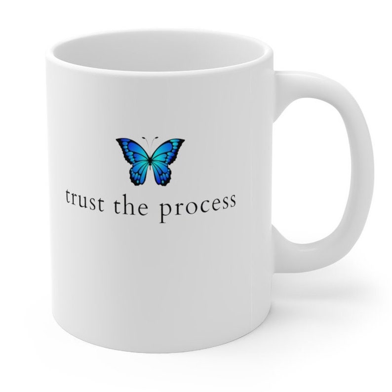 May include: White ceramic coffee mug featuring a blue butterfly graphic and the text "trust the process" printed on the front.