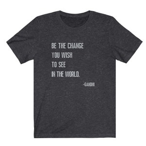 May include: Dark heather grey t-shirt with a white quote that reads "Be the change you wish to see in the world. -Gandhi".