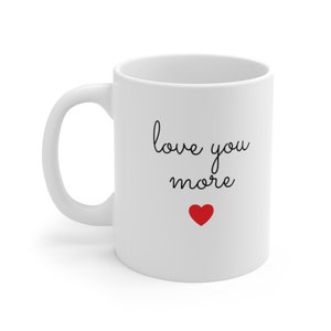 Puede incluir: Taza de caf&eacute; de cer&aacute;mica blanca con texto negro que dice "love you more" y un peque&ntilde;o coraz&oacute;n rojo.