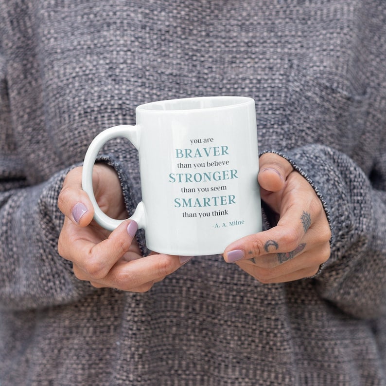 May include: White ceramic mug with a blue inspirational quote that reads "You are braver than you believe, stronger than you seem, smarter than you think - A.A. Milne".