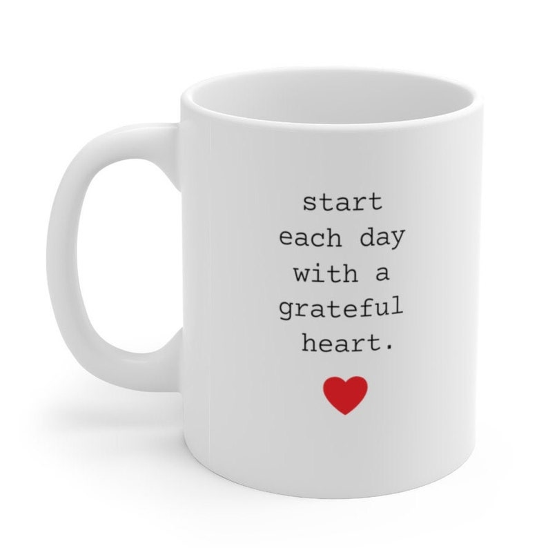 May include: White ceramic mug with a black text message that reads "start each day with a grateful heart." A red heart is below the text.