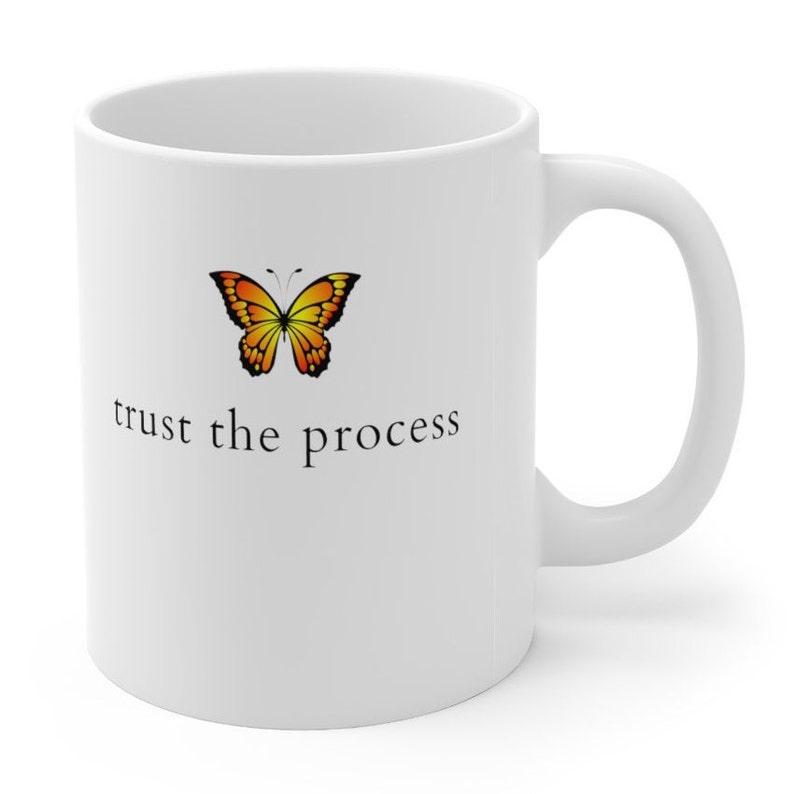 May include: White ceramic coffee mug with a yellow and orange butterfly graphic and the text "trust the process" printed in black.