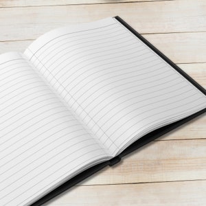 May include: A black notebook with lined pages is open and lying flat on a light wood surface.