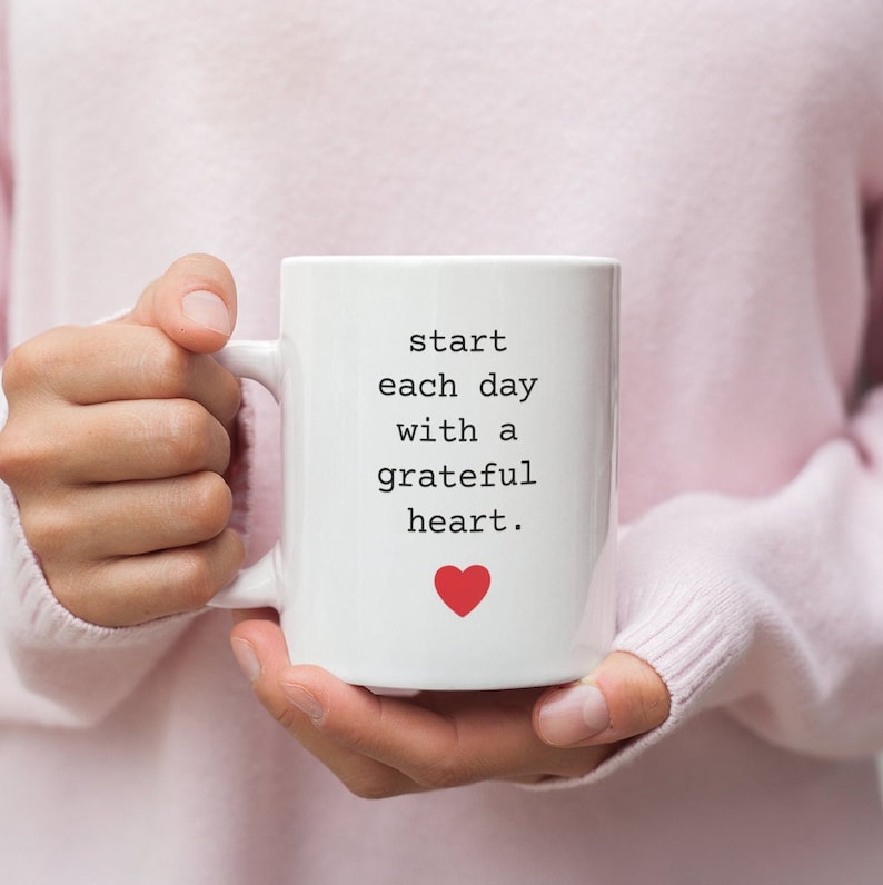 May include: White ceramic mug with a black text that reads "start each day with a grateful heart." A red heart is below the text.