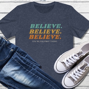 May include: A navy blue t-shirt with the words "Believe. Believe. Believe. You're halfway there." printed in a retro style with orange, blue, and green colors.