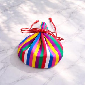 May include: A colorful drawstring pouch with vertical stripes in rainbow hues of red, yellow, green, blue, and purple. The pouch is tied with a red cord. The bag is likely used for carrying small items.
