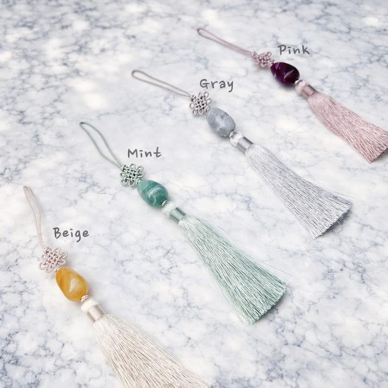 May include: Four decorative tassels in beige, mint, gray, and pink. Each tassel features a gemstone bead, a silver-colored knot, and a matching silky tassel. The colors are labeled on the image.