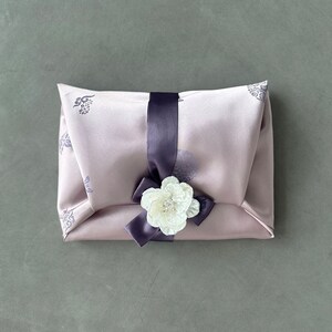May include: A light purple gift box with a white flower and a dark purple ribbon. The box has a floral pattern.