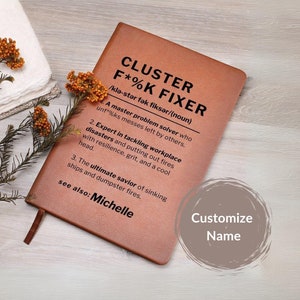 May include: A brown leather-bound journal with the title "CLUSTER F*%K FIXER" and a definition of the term. The journal has a customizable name field.