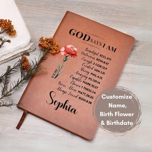 May include: A brown leather journal with the words "God Says I Am" and a list of positive affirmations with corresponding Bible verses. The journal is decorated with a pink carnation and the name "Sophia" is written in cursive at the bottom. The text "Customize Name, Birth Flower & Birthdate" is also included.