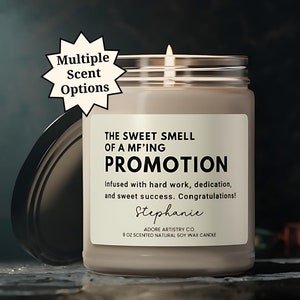 May include: A lit, scented soy wax candle in a glass jar with a silver lid. The label reads "THE SWEET SMELL OF A MF'ING PROMOTION" with a personalized name. The candle is 9 oz and has multiple scent options.