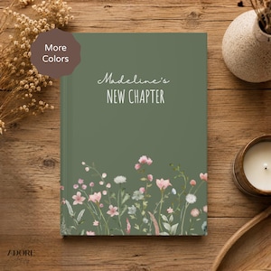 May include: A sage green hardcover book with the text "Madeline's NEW CHAPTER" printed in white. The bottom of the cover features a botanical illustration of various wildflowers in shades of pink, white, and green. A brown badge says "More Colors".