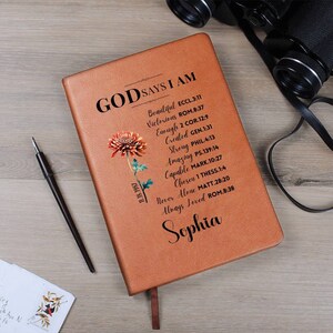 May include: A brown leather journal with the text "God Says I Am" and a list of bible verses. The journal has a floral design and the name "Sophia" is written at the bottom.