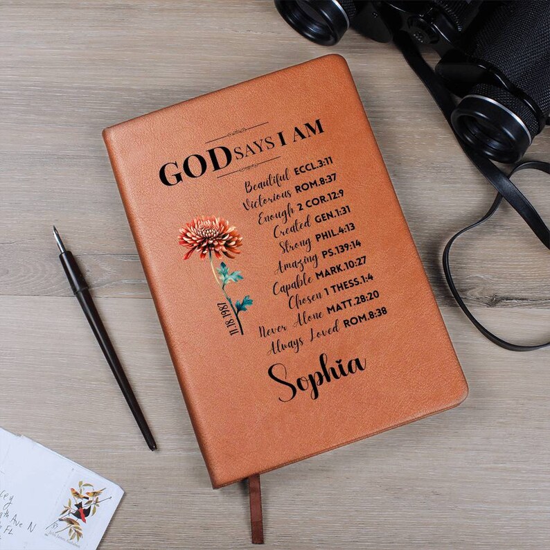 May include: A brown leather journal with the text "God Says I Am" and a list of bible verses. The journal has a floral design and the name "Sophia" is written at the bottom.