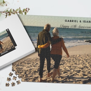 May include: A personalized 525-piece jigsaw puzzle featuring a couple walking on a beach, with the text "Gabriel & Isabel Happy 40th Anniversary" and a date. The puzzle is in a white box with a photo of the puzzle on the lid.