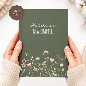 Puede incluir: Un diario de tapa dura en color verde oliva oscuro con el texto blanco "Madeline's NEW CHAPTER" y una colorida ilustración botánica de varias flores silvestres y vegetación en la parte inferior de la portada.
