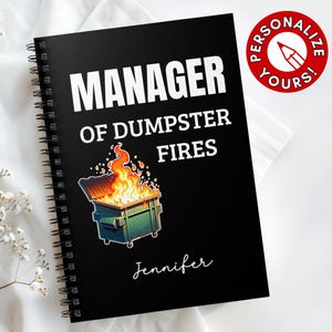 May include: Black spiral-bound notebook with the text "MANAGER OF DUMPSTER FIRES" in white. A cartoon dumpster on fire is featured below the text. The name "Jennifer" is written in cursive. A red circle with a pencil graphic says "Personalize Yours!"