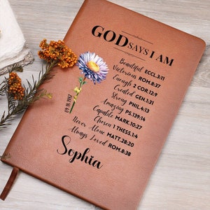 Puede incluir: Un diario de cuero marr&oacute;n con las palabras "Dios dice que soy" y una lista de vers&iacute;culos b&iacute;blicos. El diario tiene un dise&ntilde;o floral y el nombre "Sophia" est&aacute; escrito en la parte inferior.