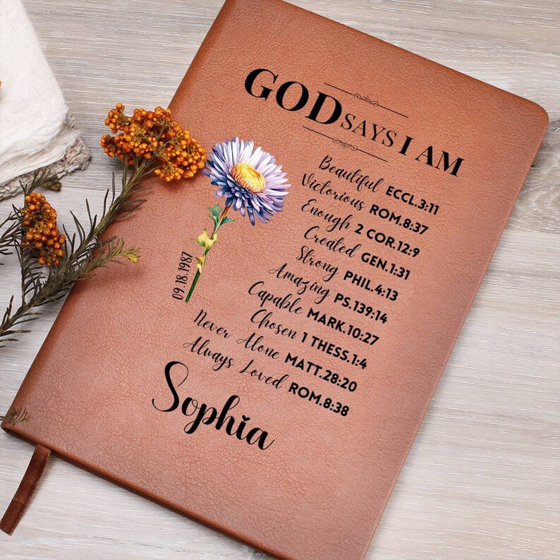 Puede incluir: Un diario de cuero marr&oacute;n con las palabras "Dios dice que soy" y una lista de vers&iacute;culos b&iacute;blicos. El diario tiene un dise&ntilde;o floral y el nombre "Sophia" est&aacute; escrito en la parte inferior.