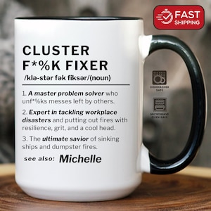 May include: White ceramic mug with a black handle and rim, featuring the text "CLUSTER F*%K FIXER" and a definition. The mug is dishwasher and microwave safe. Includes the text "see also: Michelle".