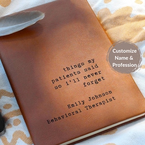 May include: A brown leather journal with the text "things my patients said so I'll never forget" and the name "Emily Johnson, Behavioral Therapist" printed on the cover. A feather rests on the journal.