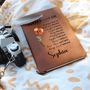 May include: A brown leather journal with the words "God Says I Am" and a list of positive affirmations and bible verses. The journal is decorated with a red poppy flower and the name "Sophia" is written at the bottom.