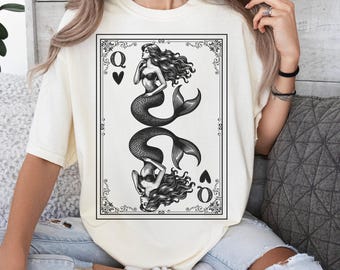 May include: Ivory-colored t-shirt featuring a black and white illustration of two mermaids in a playing card design. The card shows the Queen of Hearts symbol. The shirt has a relaxed fit.